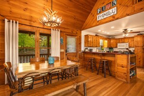 A wooden cabin interior with a dining table, chairs, a chandelier, a kitchen with wooden cabinets, and a sign that reads 'RUM Family.' - Call of the Wild, Blue Ridge, GA (Morganton)