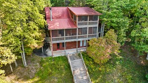 A two-story log cabin with a red roof, a balcony, and a wooden deck leading to the entrance. - Call of the Wild, Blue Ridge, GA (Morganton)