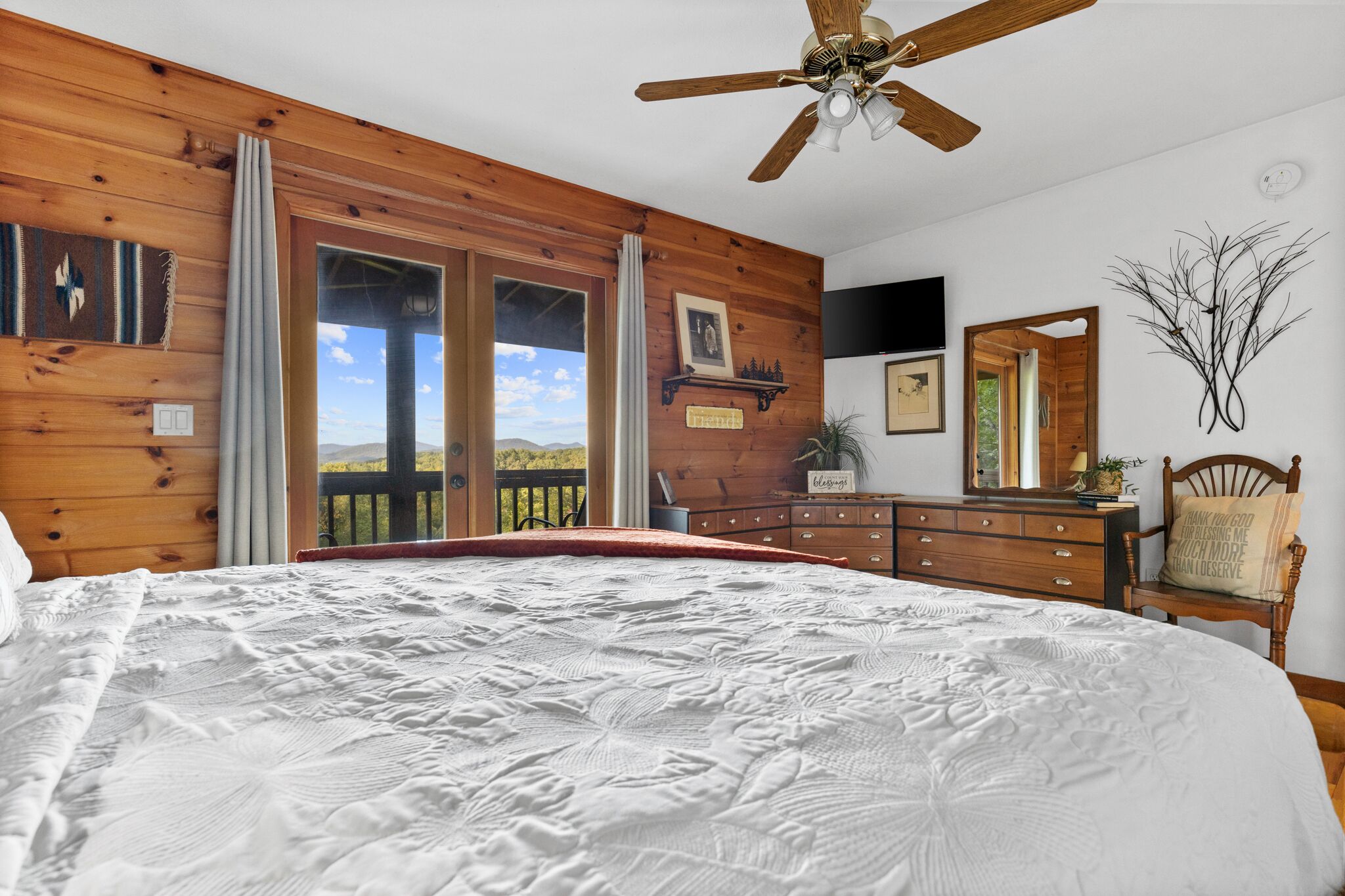 Ein Schlafzimmer mit einem großen Bett, Holzwänden, einem Deckenventilator, einem Schminktisch, einem Spiegel und Blick ins Freie.