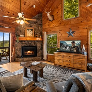 Interior acogedor de una cabaña con chimenea, paredes de madera, cabeza de venado decorativa, televisor y adorno con forma de estrella.
