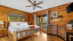 A wooden cabin bedroom with a bed, dresser, and ceiling fan. - Call of the Wild, Blue Ridge, GA (Morganton)