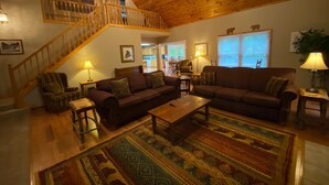 A spacious living room with a wooden ceiling, a staircase, a large sofa, a coffee table, and a patterned rug. - North Georgia Cabin, Sleeps 8, Pet Friendly (Morganton)