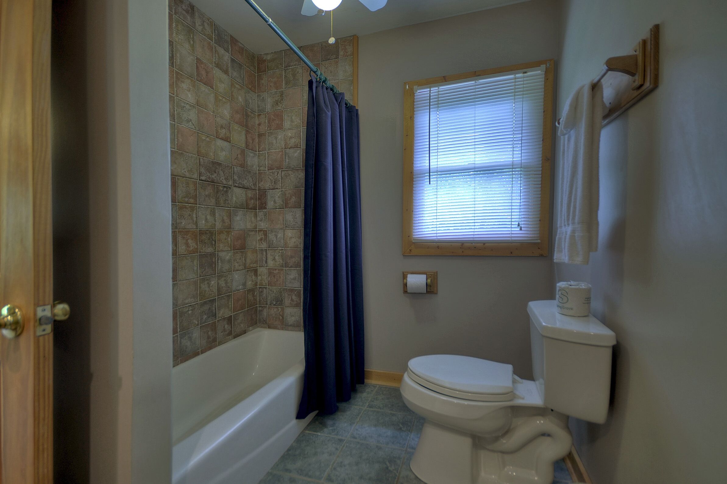 Un baño con bañera, inodoro y ventana con persianas.