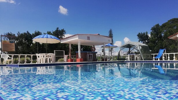 En swimmingpool med blå og hvide mosaikfliser, omgivet af hvide stole og parasoller.