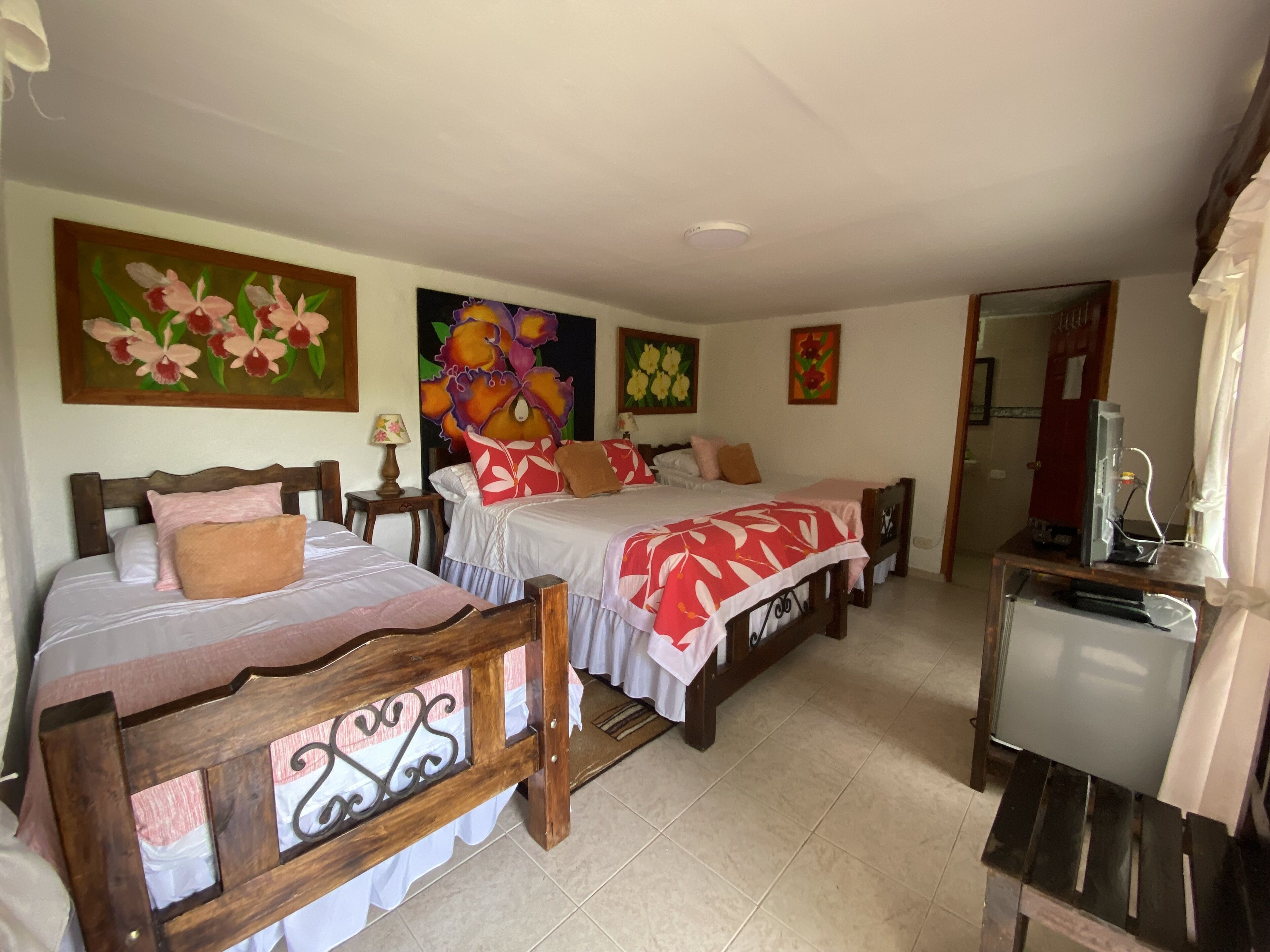 A hotel room with two beds, a desk with a computer, and floral artwork on the walls.