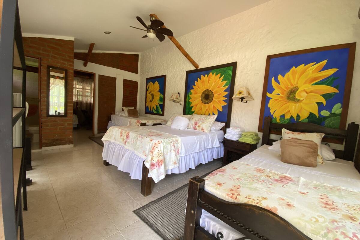 Ein Hotelzimmer mit zwei Betten, einem Deckenventilator und großen Sonnenblumengemälden an den Wänden.