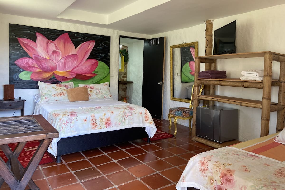 Ein Hotelzimmer mit einer großen Blumenwand, einem Bett mit floraler Bettwäsche, einem Holzregal mit Handtüchern, einem Fernseher und einem kleinen Tisch.