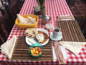 A table set with a checkered tablecloth, a basket, a cup of coffee, a plate with food, and a bowl of fruit. - Finca Hotel Villaluzandi (Alcalá)