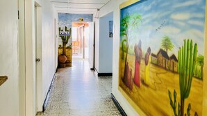 Un couloir orné d’une fresque représentant un paysage désertique, doté d’un sol carrelé et de portes situées sur le côté gauche.