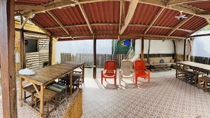 Une terrasse extérieure couverte, dotée de meubles en bois, d’un sol carrelé et d’une esthétique rustique.