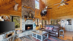 Interior acogedor de una cabaña con chimenea de piedra, mobiliario de cuero y trofeos de animales colgados.