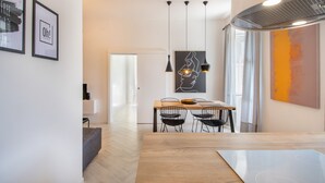 Ein moderner Essbereich mit einem Holztisch, schwarzen Drahtstühlen, Pendelleuchten und Kunstwerken an den Wänden.
