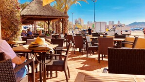 An outdoor seating area with wicker furniture, a thatched-roof structure, and a view of the city skyline. - Luxury Apartment with pool by Poniente beach (Benidorm)