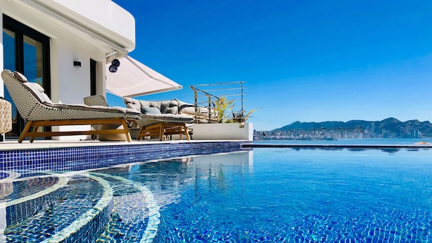 A poolside area with lounge chairs and a view of a cityscape. - Luxury Apartment with pool by Poniente beach (Benidorm)
