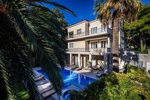 A two-story house with a swimming pool, surrounded by lush greenery and palm trees. - Villa Diocletian (Split)