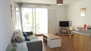 A modern living room with a sofa, coffee table, TV, and a small kitchen area with a counter and chairs.