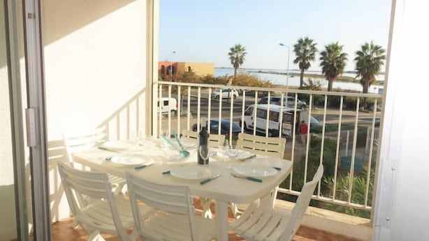 A balcony with a table set for four, white chairs, and a view of parked cars and palm trees.