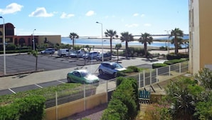 A parking lot with several cars and a green car in the foreground. There are palm trees and a building with a red facade in the background.