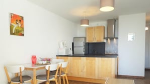 A compact kitchen with wooden cabinets, a white countertop, and a dining area with a table and chairs.