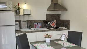 A compact kitchen with a microwave, sink, and stove. There is a dining table with chairs and a small potted plant.