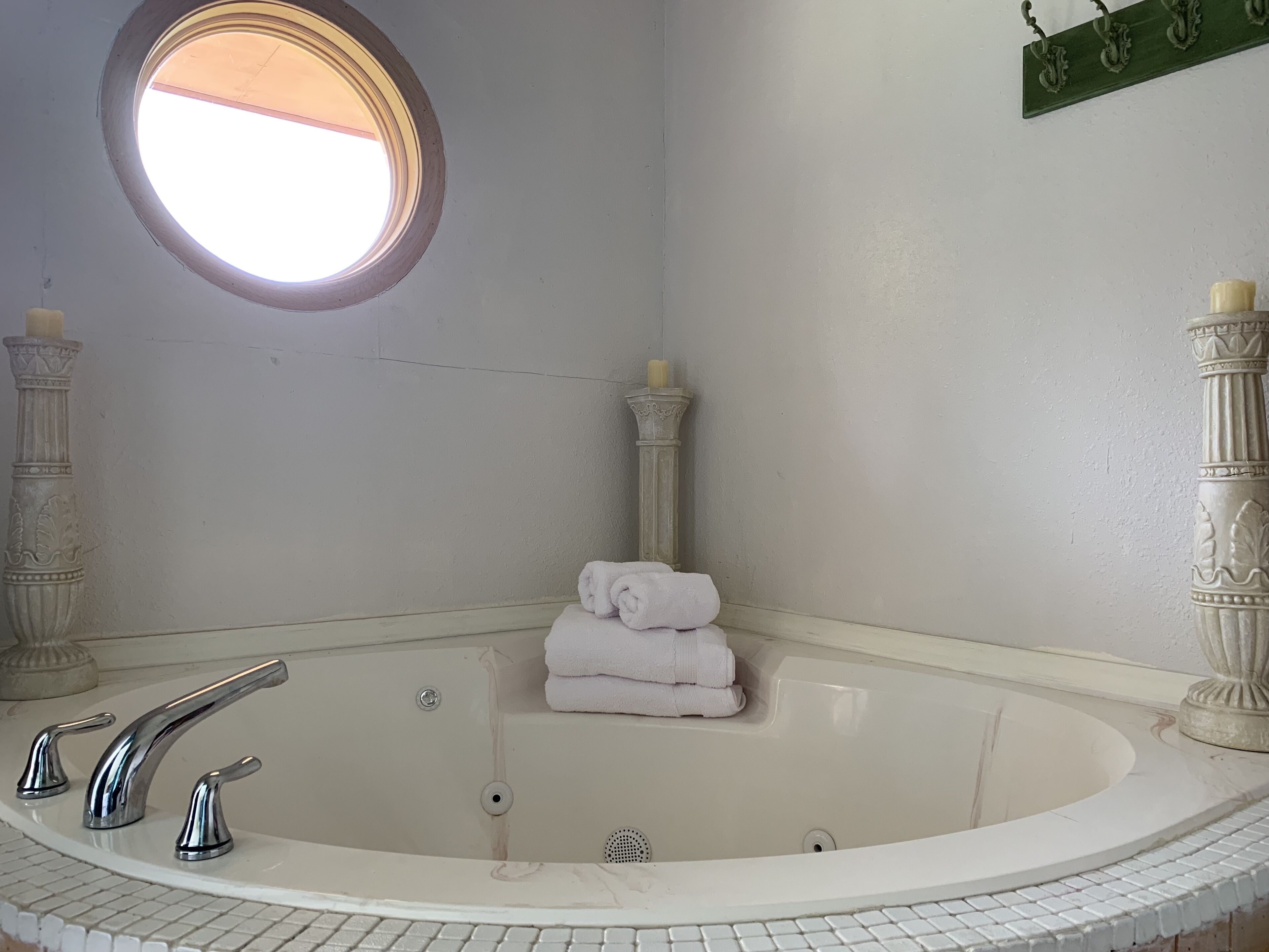 Un baño con una bañera grande, un espejo redondo y dos columnas.