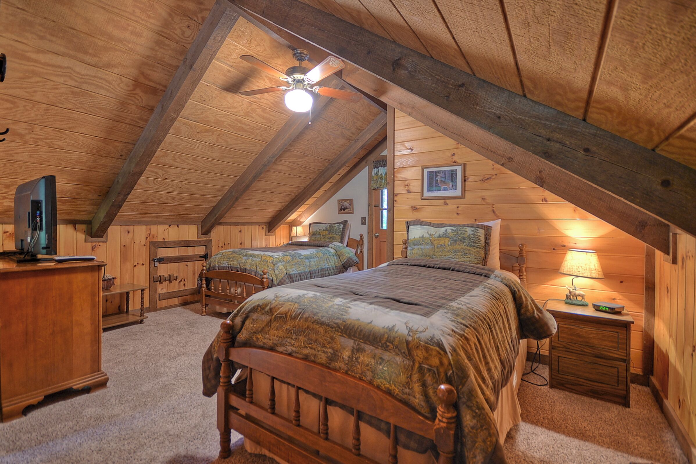 Een gezellig slaapkamer op zolder met twee houten bedden, een plafondventilator en een houten dressoir.