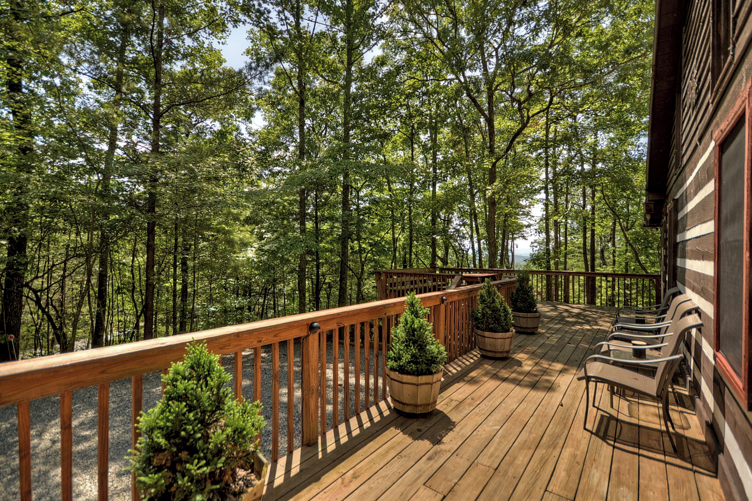 A wooden deck with a railing, potted plants, and outdoor seating.
