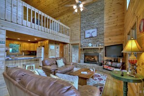 A spacious living area with a fireplace, a television, and a kitchen in the background.