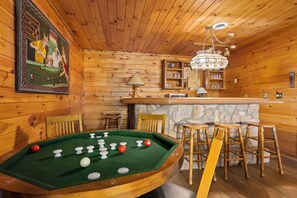 A wooden room with a pool table, bar stools, and a stone fireplace.