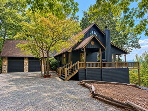 Une maison à deux étages avec un garage en pierre, une véranda en bois et une allée gravillonnée.