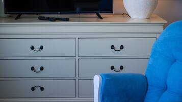 A television on a white dresser, a blue chair, and a white lamp.