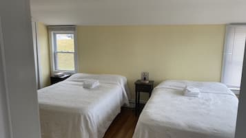 A room with two beds, each with a white bedspread and folded towels. There is a small table with a lamp between the beds.