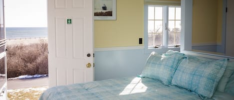 A bedroom with a bed, a door leading outside, a window, and a framed picture on the wall.