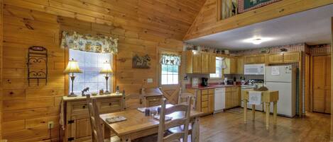 A wooden cabin interior with a dining area, kitchen, and a loft bedroom.