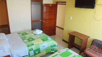 A hotel room with two beds, a television mounted on the wall, a wooden wardrobe, and a small table.