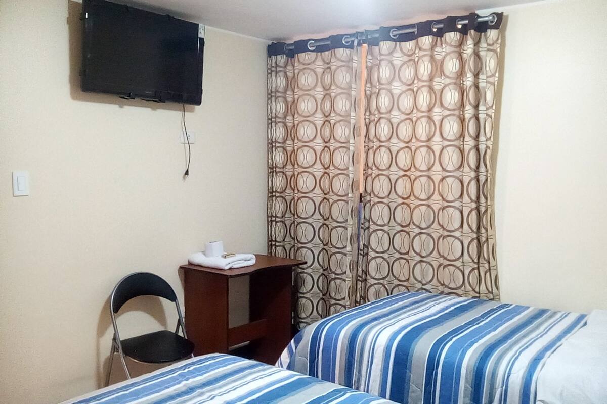 Een kamer met twee bedden, een bureau, een stoel, een televisie en gordijnen met een patroon.