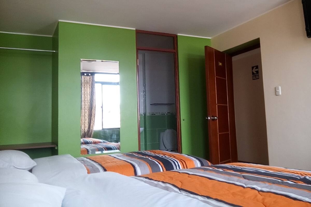 Een kamer met groene wanden, een bed met gestreepte beddengoed, een kledingkast en een spiegel.