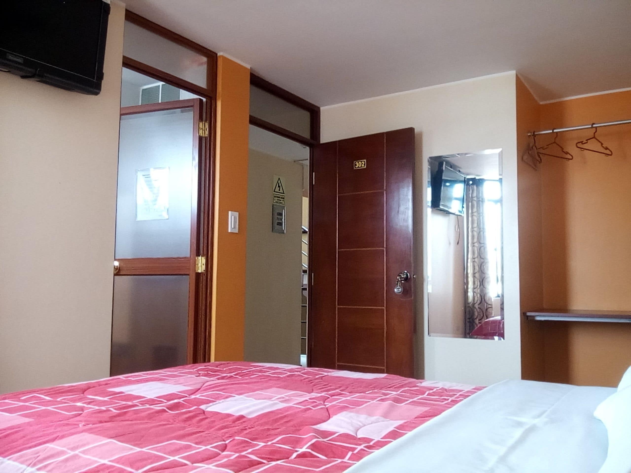 Una habitación de hotel con cama, puerta, espejo y perchero.