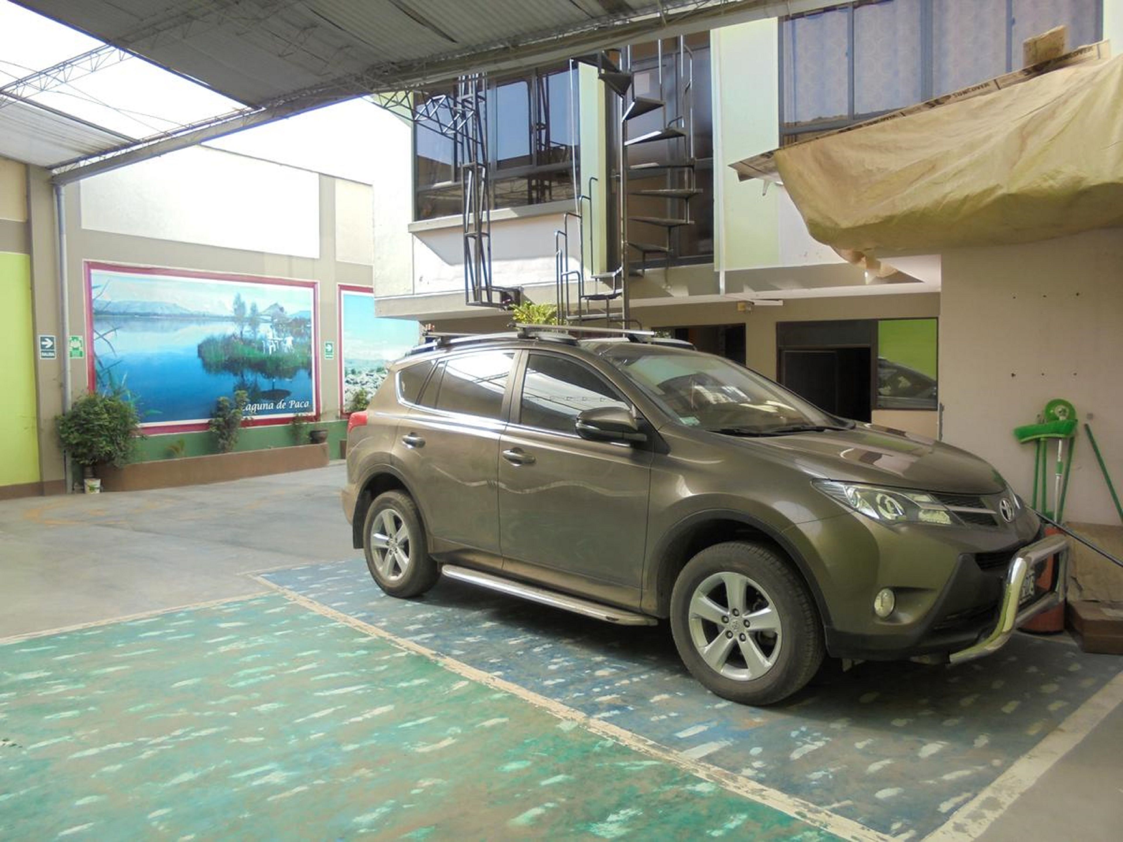 Un automóvil estacionado en un área de estacionamiento techada, con vista a un edificio y un cartel en el fondo.