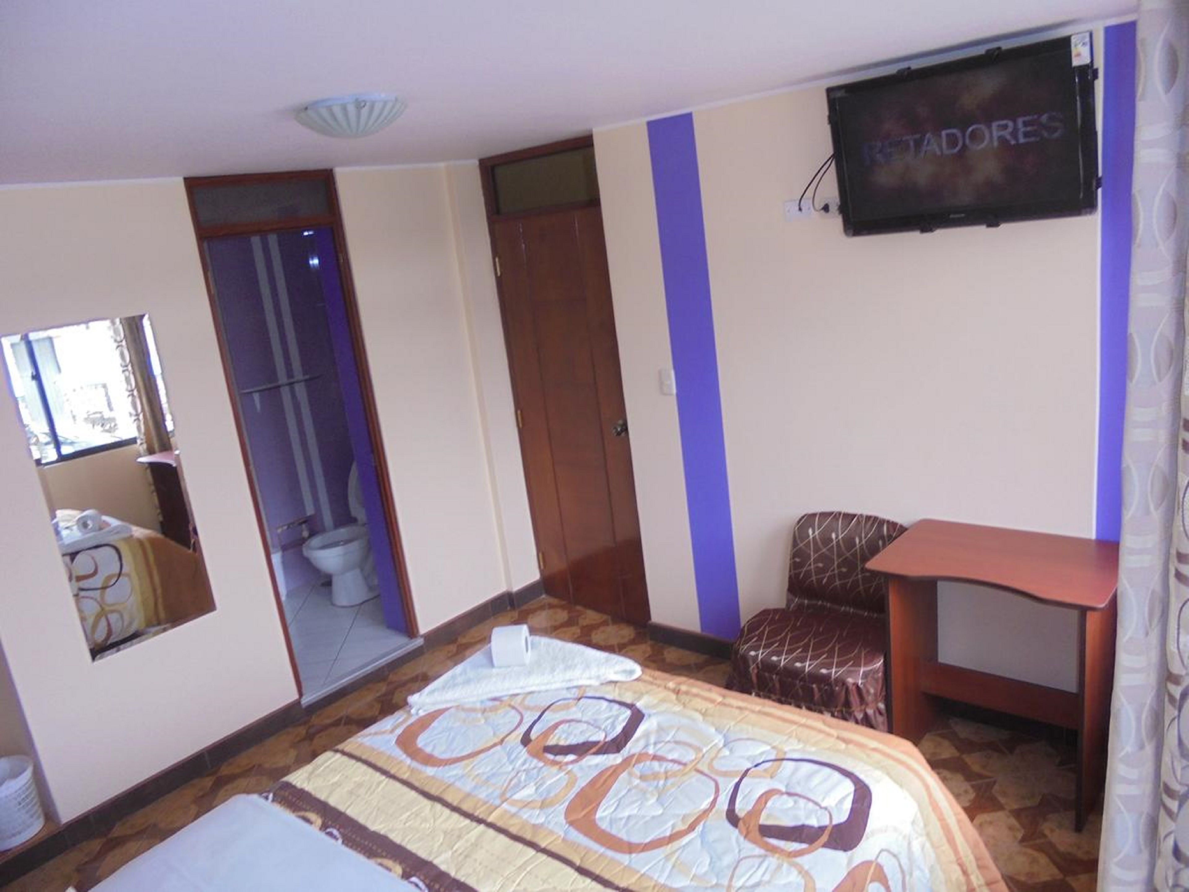 A hotel room with a bed, a television, a chair, and a bathroom visible through an open door.