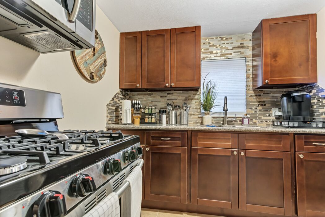 A kitchen with wooden cabinets, a gas stove, and a tiled backsplash.