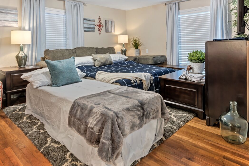 A bedroom with two beds, a wooden dresser, a nightstand, a lamp, and a plant.