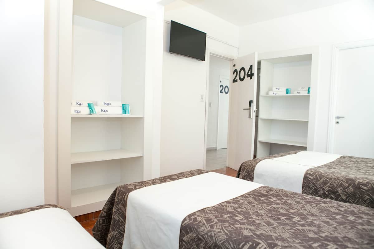 A hotel room with two beds, a TV mounted on the wall, and a wardrobe with shelves.