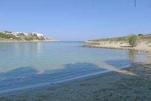 Een strand met helder water, een zandstrand en gebouwen op de achtergrond.