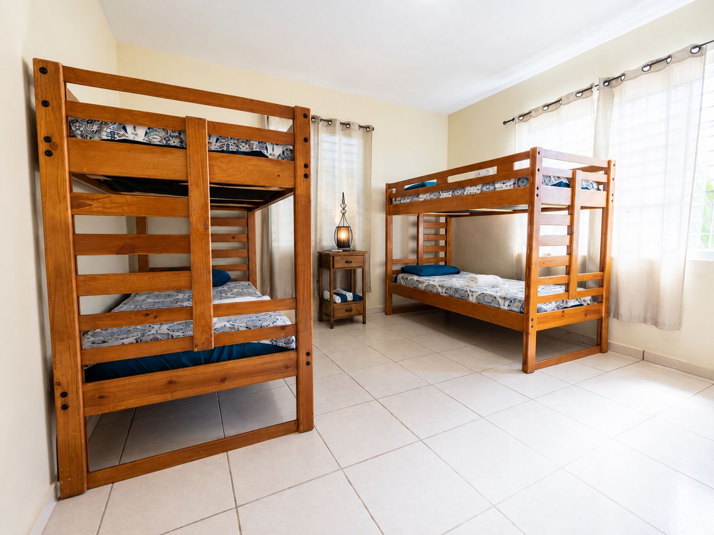 Una habitación con dos literas, una mesita con lámpara y una ventana con cortinas.