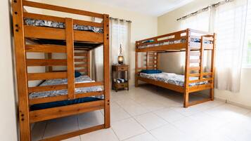 Una habitación con dos literas, una mesita con lámpara y una ventana con cortinas.