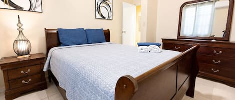A bedroom with a bed, a nightstand, a dresser, a mirror, and two abstract paintings on the wall.