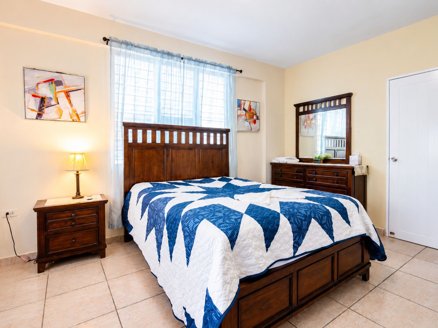 Un dormitorio con una cama de madera, una mesita de noche con lámpara, un aparador y un espejo.