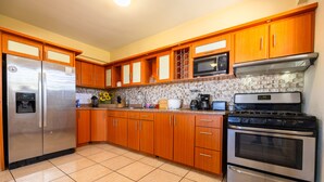 A kitchen with wooden cabinets, a stainless steel refrigerator, a microwave, a stove, and a tiled floor. - Colinas del Atlantico for 18 People (Isabela)