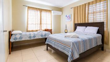 A hotel room with two beds, a ceiling fan, and a wall-mounted air conditioner.